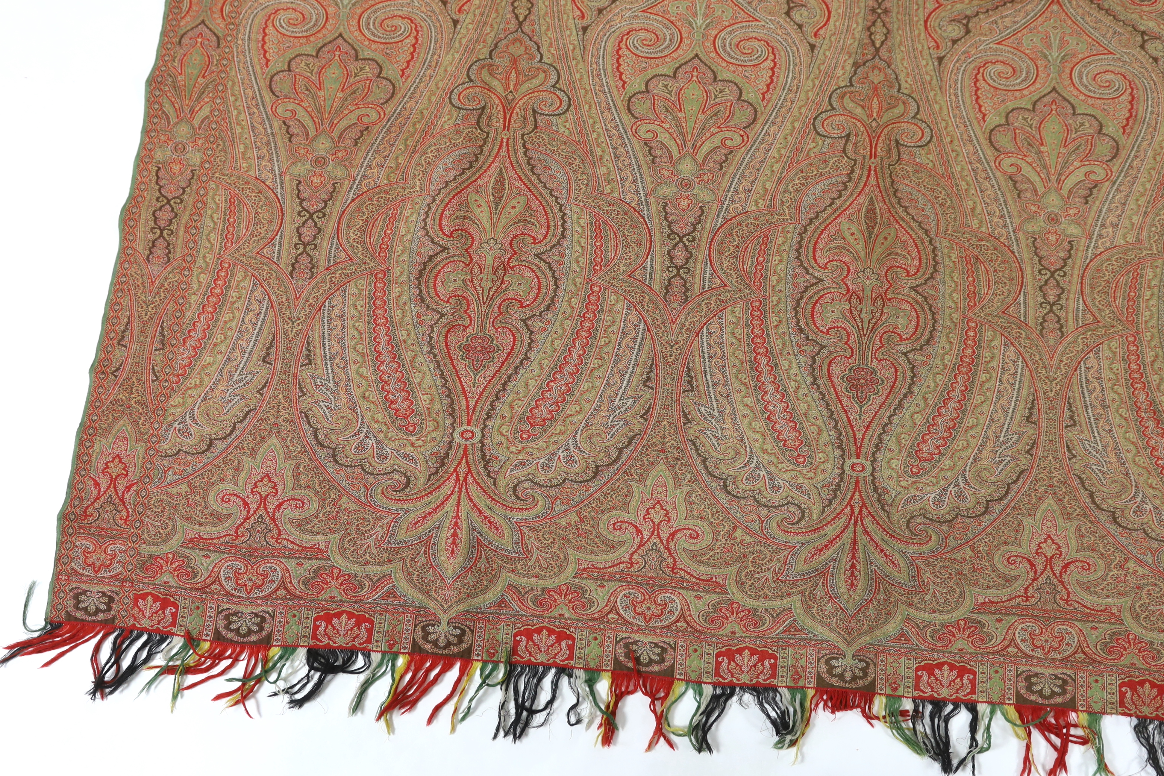 An 1860’s, reversible woven wool Paisley shawl, woven with green, red, ochre and brown, with a woven border and fringing both ends. 166cm wide x 169cm long
